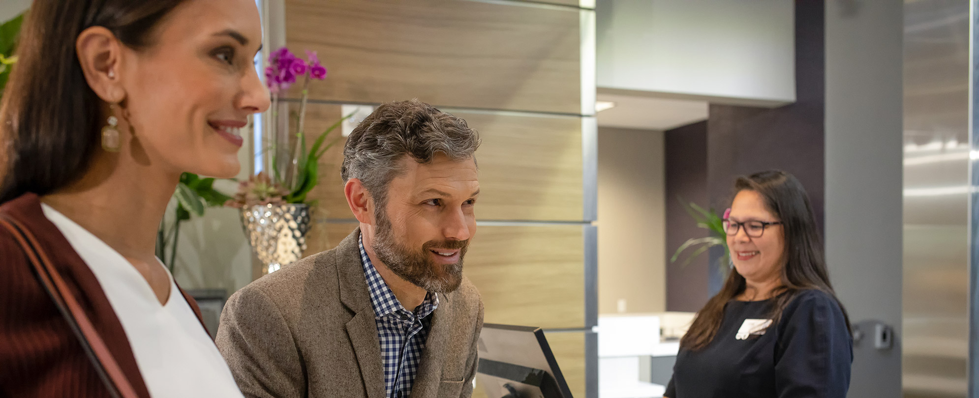 A smiling man and woman have a conversation with a front desk agent at a Club Wyndham resort.