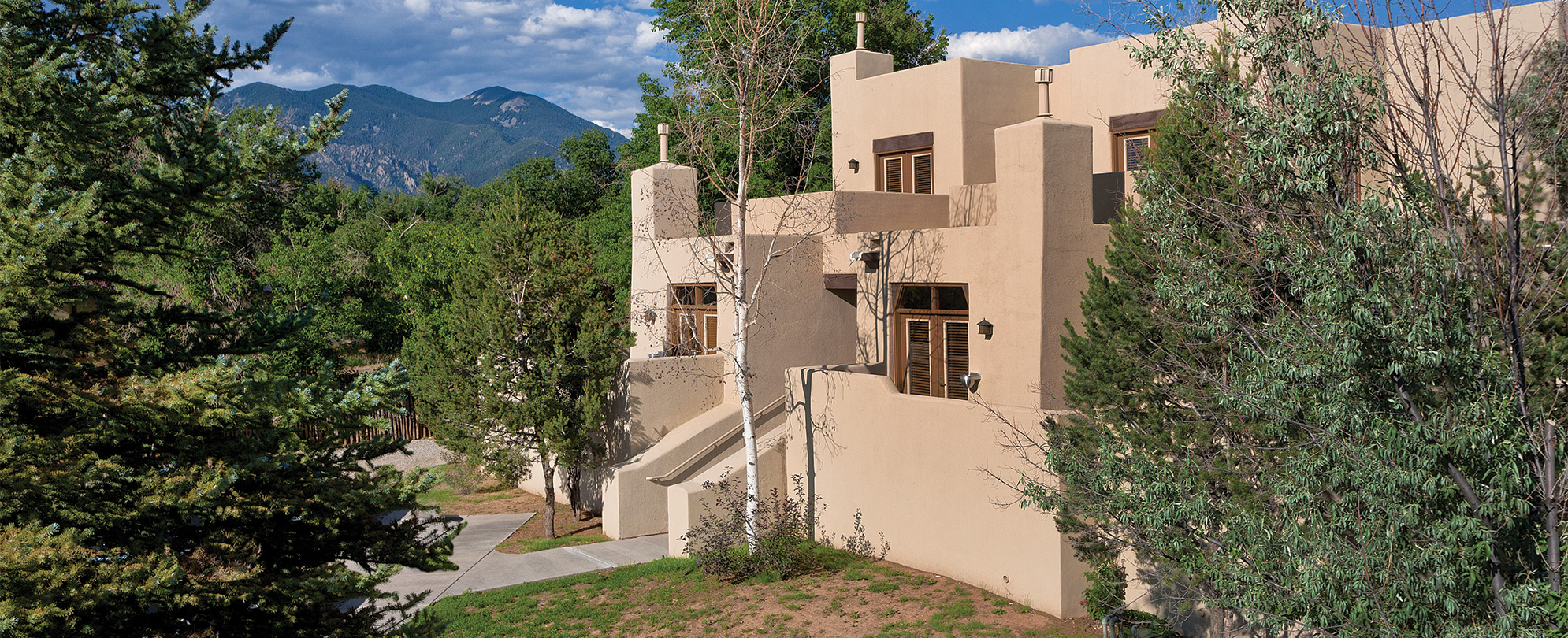 The exterior of Club Wyndham Taos, a timeshare resort in Taos, New Mexico, surrounded by trees and mountains.