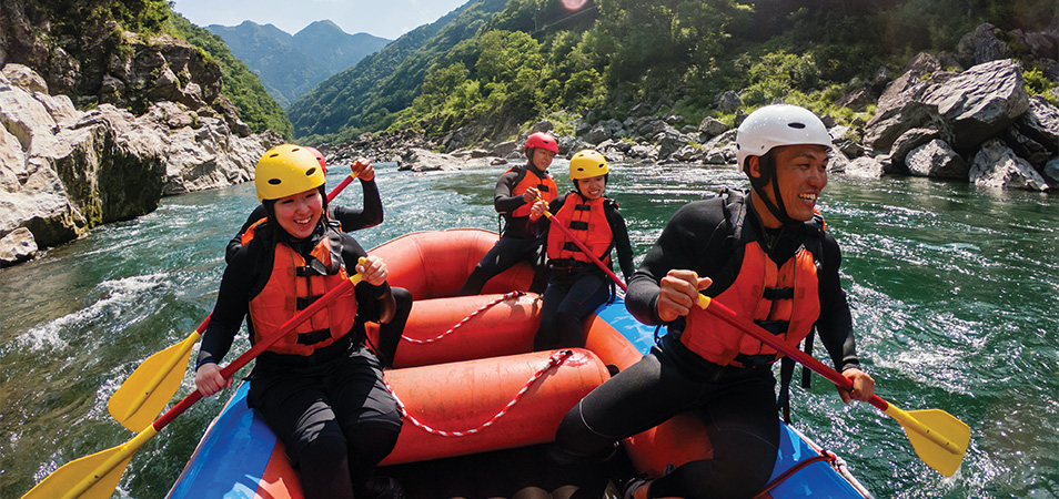 A group of five paddling on a raft that is floating down a river.