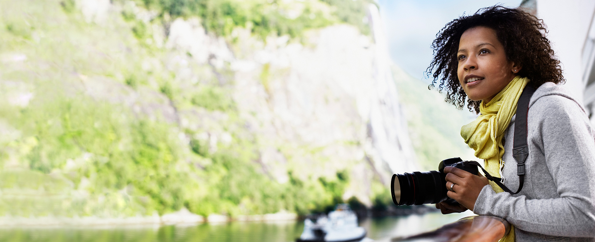 Woman holding a camera and looking out at the view from a river cruise balcony. 