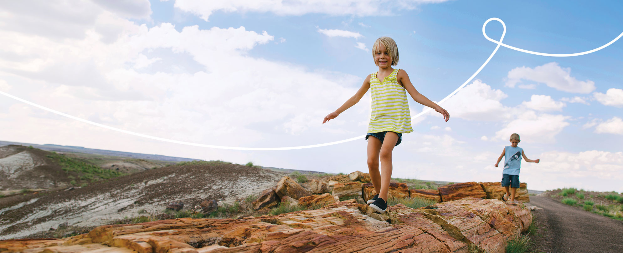 A little girl and her brother walking along a path of red rocks on the side of a mountain trail. 