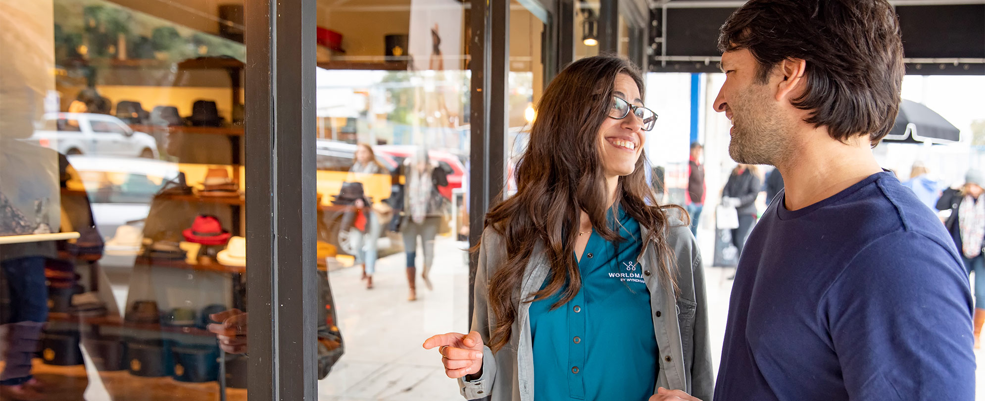 A man and woman stand smiling in front of a store window.