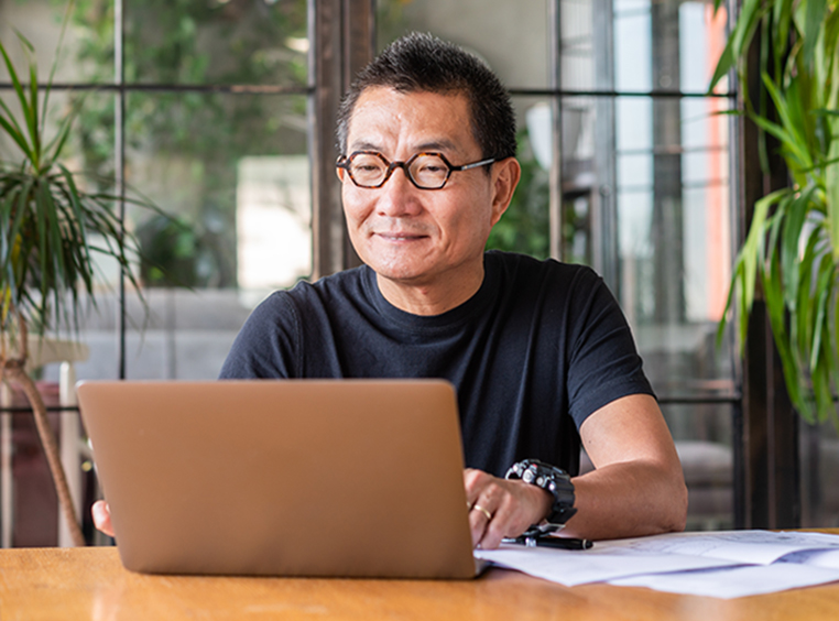 An older man sitting at a table and looking at his laptop. 