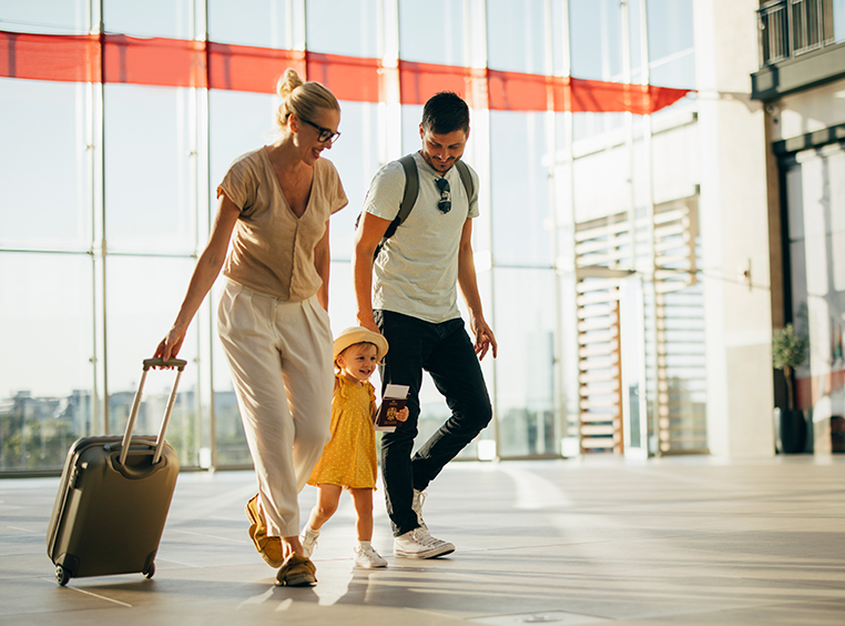 A family of three walking through the airport with their luggage.