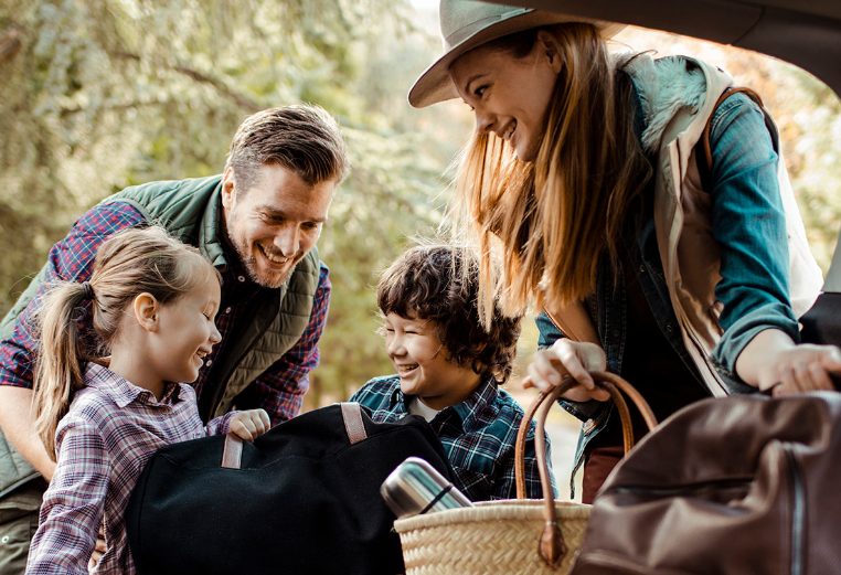 Mom, dad, and two young kids put suitcases and backpacks in the backseat of a car for their WorldMark by Wyndham vacation.