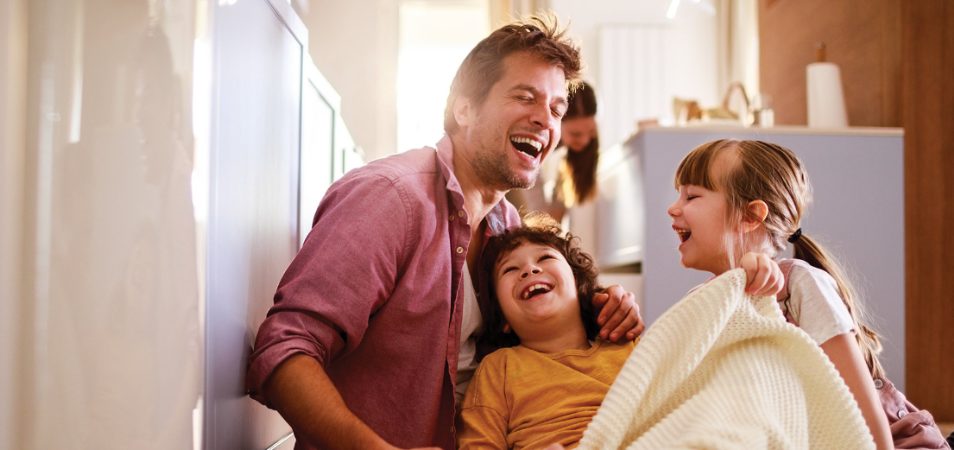 A dad sits with his young son and daughter beside him, they are all laughing and enjoying a WorldMark by Wyndham vacation.