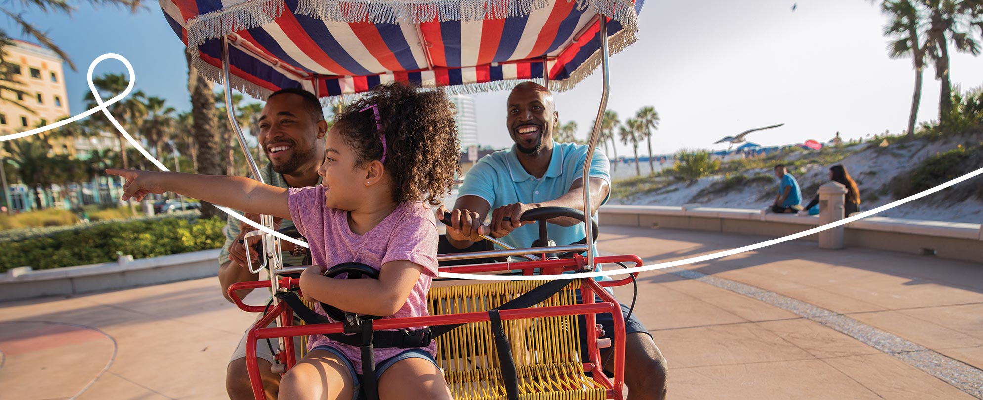 Two men and their daughter ride on a multiperson bike, the little girl points to something in the distance.