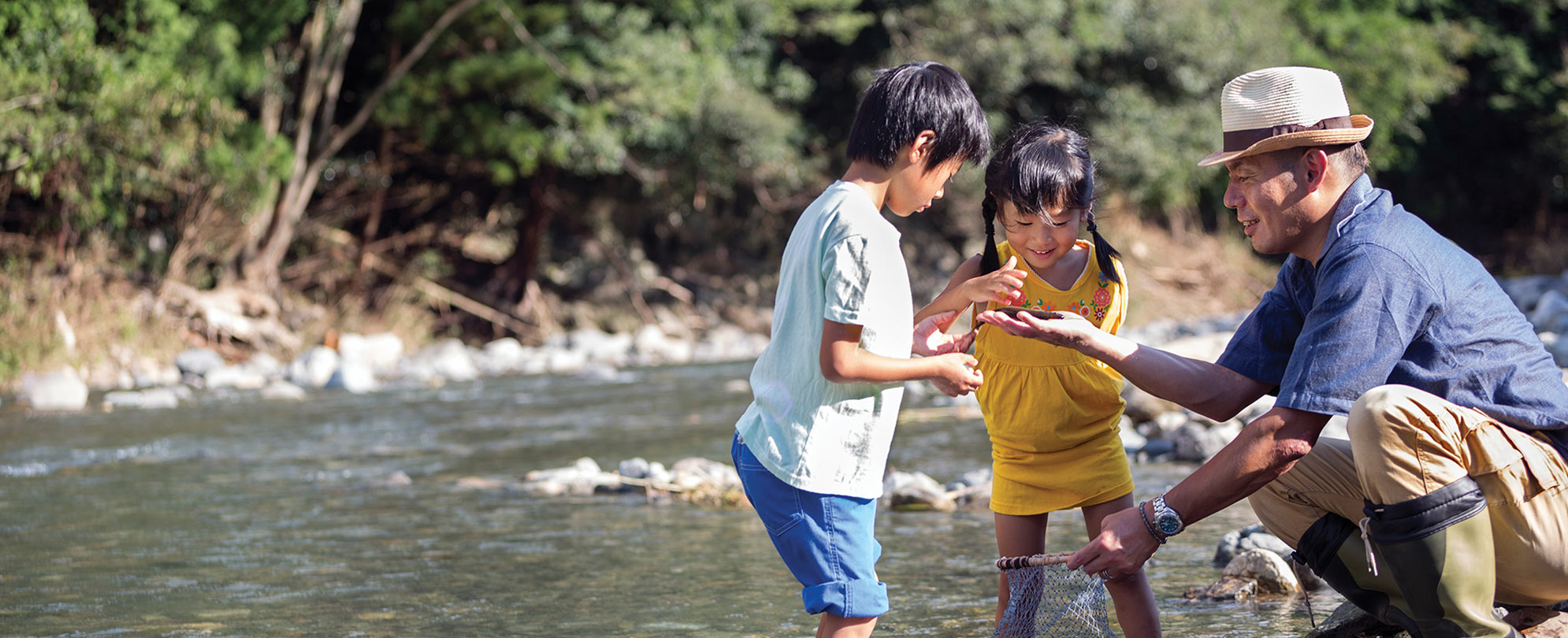 Two kids and their father with their feet in the water looking at something in their father's hand.