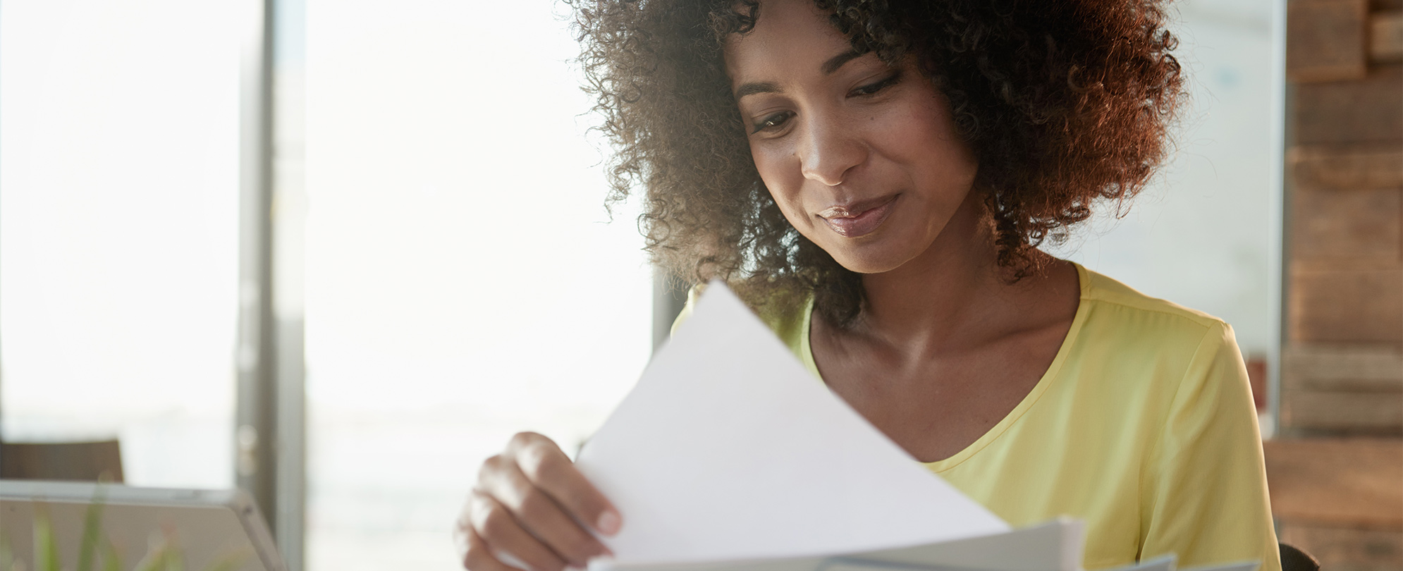 A woman with curly hair smiles looking down at the papers she is holding.