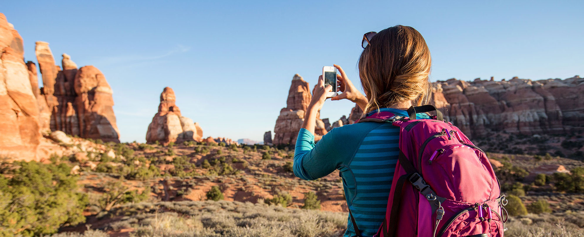 A woman stops along the side of the road and opens up her car door to look out onto the red rock formations in Utah.