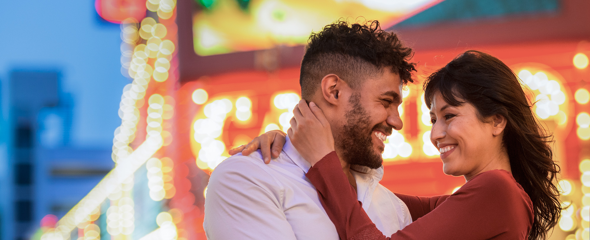 A smiling couple embraces and looks into each other's eyes with the bright lights of Las Vegas in the background.