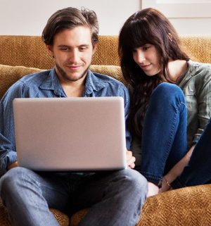 A man and woman sit comfortably on a couch looking at a computer, reading the latest news from WorldMark by Wyndham.