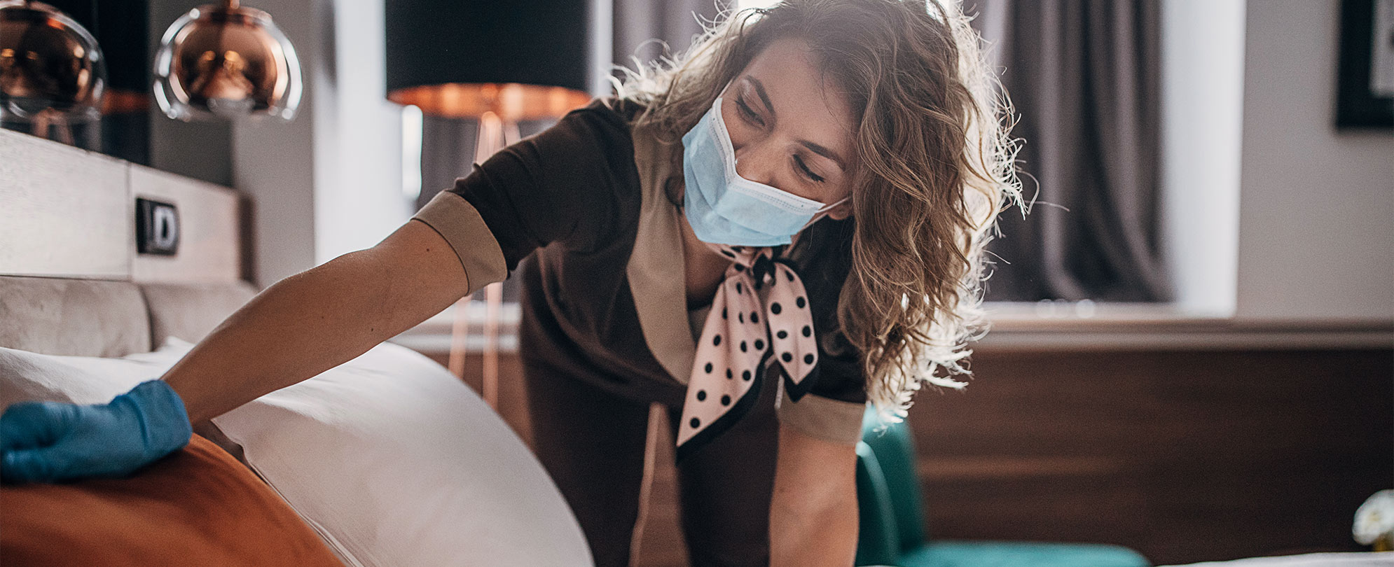 A WorldMark by Wyndham employee wearing medical mask and gloves makes the bed in a resort suite.