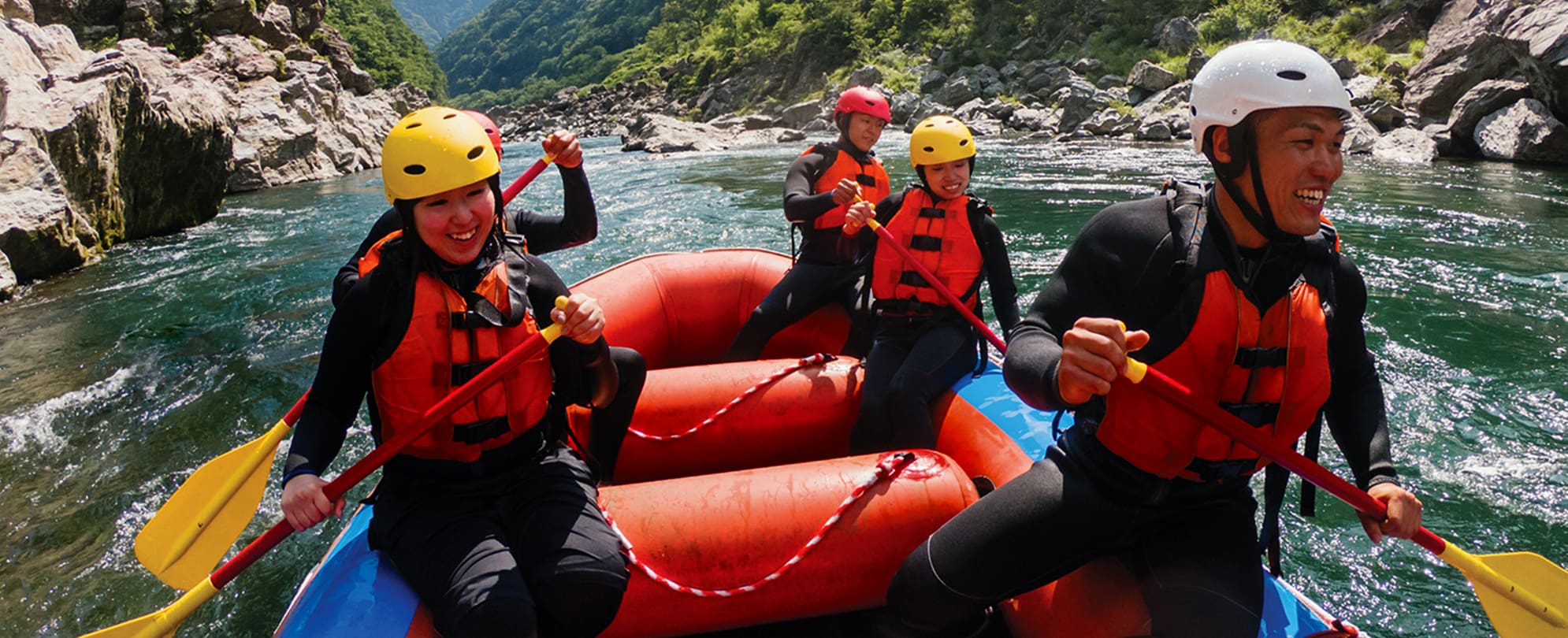 A family white water rafts in a river lined by mountains during their WorldMark by Wyndham vacation.